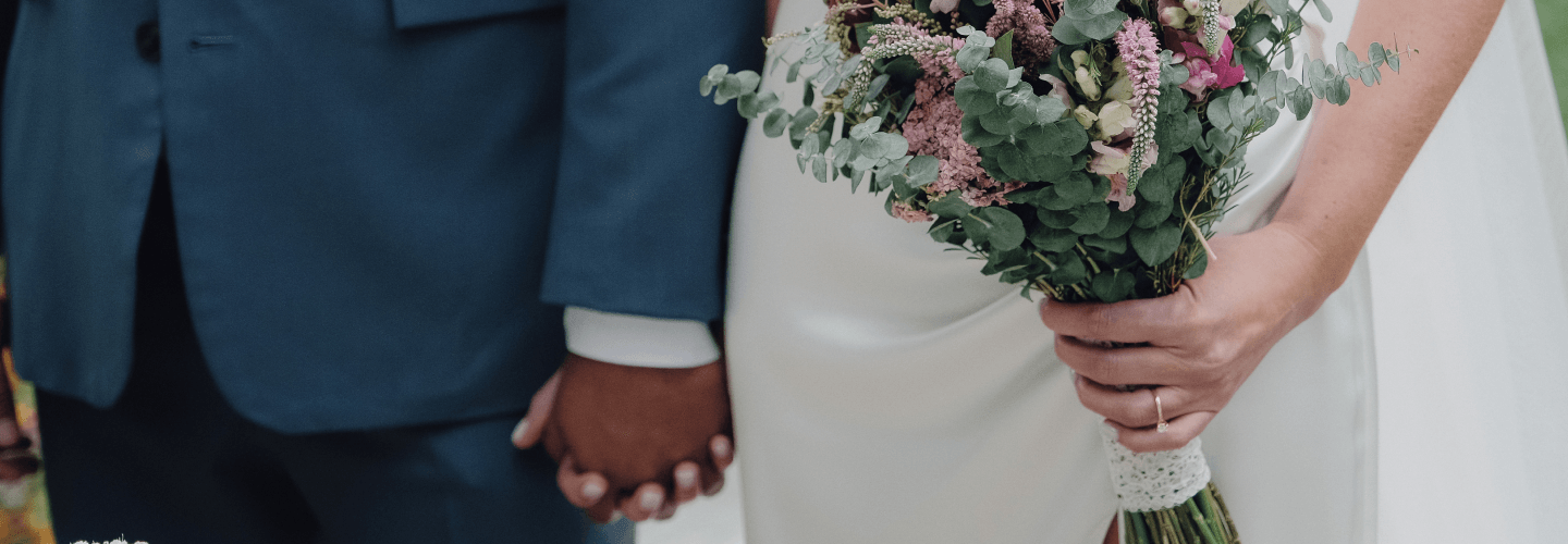 Una pareja tomada de la mano; la novia sostiene su ramo con la otra