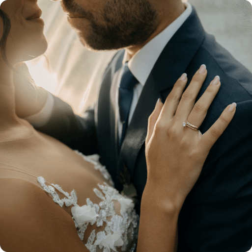 La mano de una novia, con su anillo de compromiso, apoyada en el hombro del novio